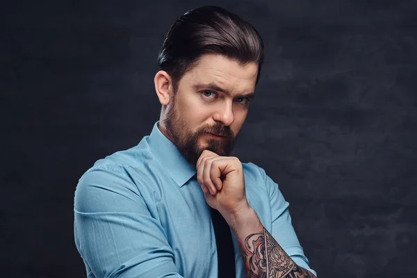Portrét pohledný tetované muže středního věku s vousy a účes oblečený v modré košili a kravatu, představují ve studiu s překřížením rukou. — Stock fotografie