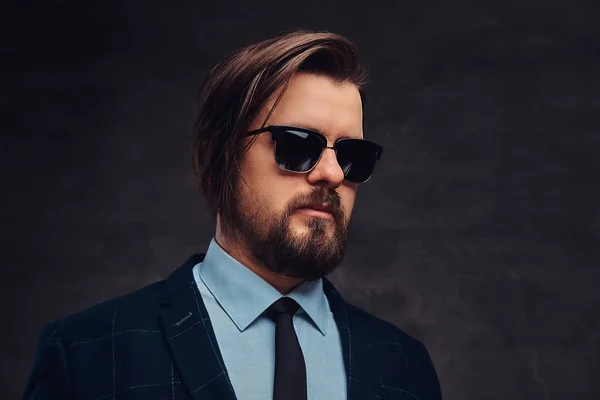 Close-up portrait of a handsome fashionable middle-aged man with beard and hairstyle dressed in an elegant formal suit and sunglasses. Isolated on a textured dark background in studio. — Stock Photo, Image