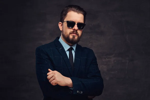 Close-up portrait of a handsome fashionable middle-aged man with beard and hairstyle dressed in an elegant formal suit and sunglasses. Isolated on a textured dark background in studio. — Stock Photo, Image