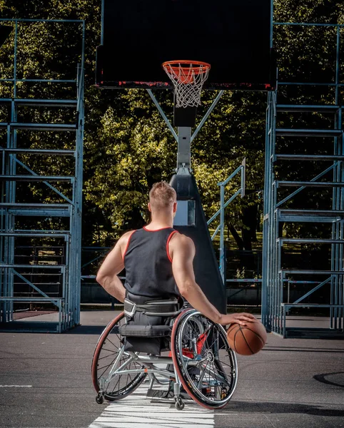 Joueur de basket-ball cramoisi dans un fauteuil roulant joue sur un terrain de jeu ouvert . — Photo