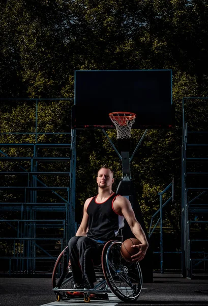 Jogador de basquete aleijado em uma cadeira de rodas segura uma bola em um campo de jogo aberto . — Fotografia de Stock