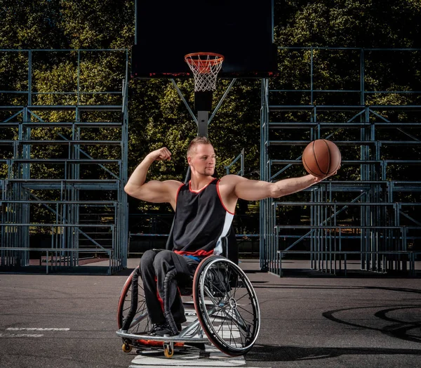 Un joueur de basket-ball handicapé souriant en fauteuil roulant tient une balle sur un terrain de jeu ouvert . — Photo