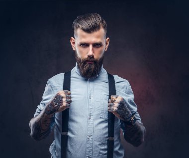 Mavi bir gömlek ve pantolon askısı yakışıklı bir eski moda hipster portresi. Karanlık bir arka plan üzerinde izole.