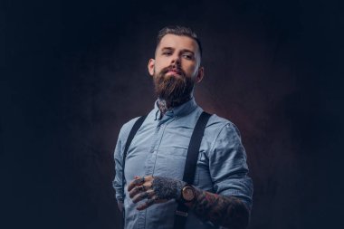 Mavi bir gömlek ve pantolon askısı yakışıklı bir eski moda hipster portresi. Karanlık bir arka plan üzerinde izole.