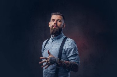 Mavi bir gömlek ve pantolon askısı yakışıklı bir eski moda hipster portresi. Karanlık bir arka plan üzerinde izole.
