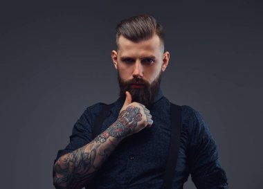 Dalgın yakışıklı eski moda hipster gömlek ve pantolon askısı, çene üzerinde el ile poz. Karanlık bir arka plan üzerinde izole.