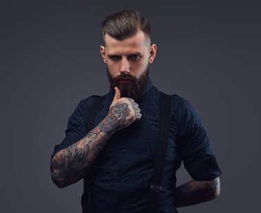 Dalgın yakışıklı eski moda hipster gömlek ve pantolon askısı, çene üzerinde el ile poz. Karanlık bir arka plan üzerinde izole.