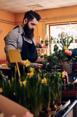 Sakal ve elinde bir çiçekçi dükkanı kasada duran güzel çiçek kompozisyon yapma dövme ile profesyonel erkek çiçekçi.