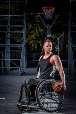 Tekerlekli sandalyede kötürüm basketbol oyuncusu bir topu açık oyun yere tutuyor..