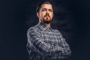 Portre sakal ve saç modeli ile orta yaş hipster birinin bir kareli gömlek giymiş, bir stüdyoda çapraz silah ile poz. Karanlık dokulu bir arka plan üzerinde izole.