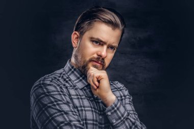 Dalgın orta yaş erkek sakal ve saç modeli ile çene yandan kareli gömlek pozuyla giymiş. Karanlık dokulu bir arka plan üzerinde izole.