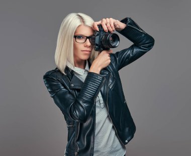 Güzellik akıllı sarışın kadın fotoğrafçı bir beyaz bluz ve siyah deri ceket bir stüdyoda fotoğraf çekme. Gri bir arka plan üzerinde izole.