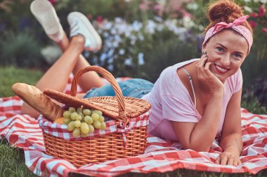 Açık havada yatarken üzerinde bir battaniyeye parkta piknik sırasında bir kafa bandı zevk ile rahat kıyafetler içinde mutlu kızıl saçlı orta yaş kadın.