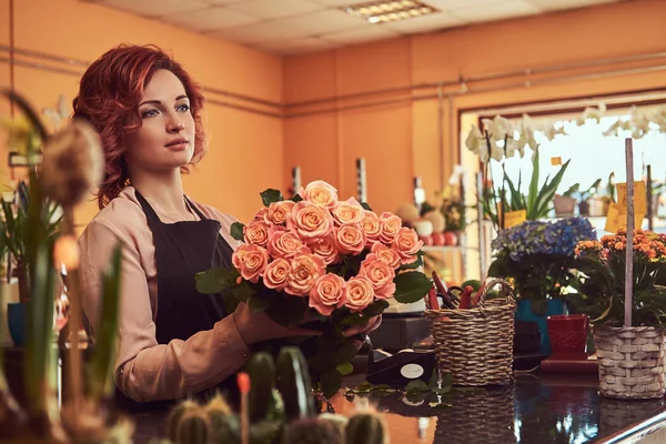Büyüleyici Kızıl saçlı kadın çiçekçi çiçekçi tezgahta duran güzel çiçek kompozisyon yapmak üniforma.
