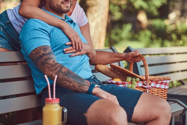 Resim bir çiftin sırasında dating, rahat kıyafetler giyen kırpılmış açık havada bir parkta bir bankta piknik.
