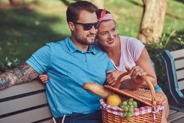 Attractive middle age couple during dating, enjoying a picnic on a bench in the park.