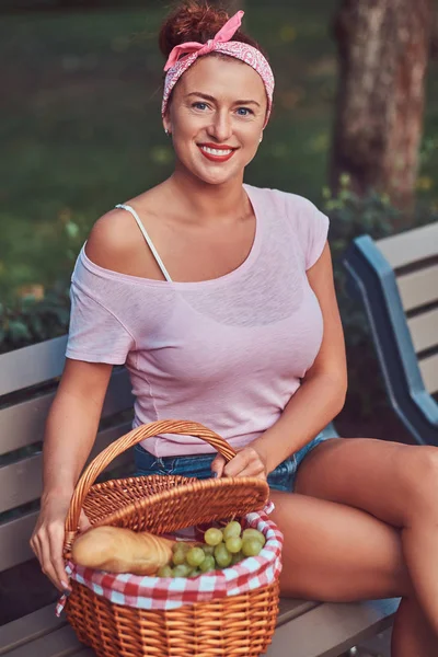 Bir piknik sepeti bir parkta bir bankta oturan rahat kıyafetler giymiş mutlu güzel kızıl saçlı erkek.