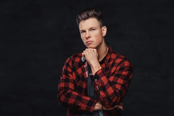 Thoughtful handsome young guy in a fleece shirt, posing with hand on chin at a studio. Isolated on a dark background.