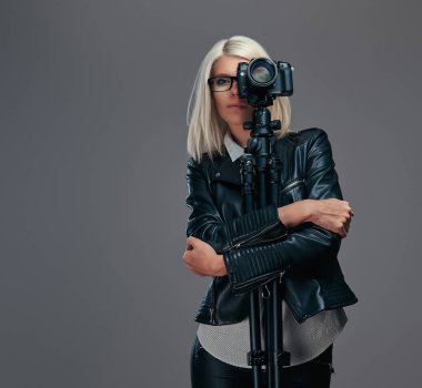 Siyah deri ceketli bir stüdyoda bir fotoğraf çekerken profesyonel bir kamera bir tripod ile sarılma gözlük güzellik akıllı sarışın kadın fotoğrafçı.