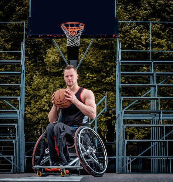 Cripple basketball player in a wheelchair holds a ball on an open gaming ground.