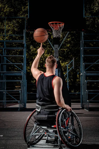 Баскетболист-инвалид в инвалидной коляске крутит баскетбольный мяч на пальце на открытой игровой площадке . — стоковое фото