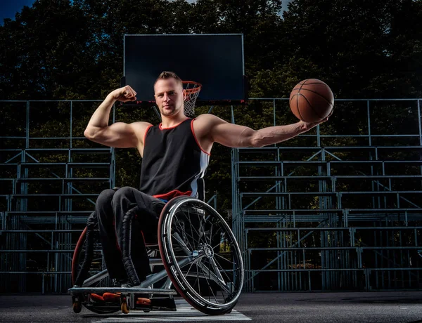 Jogador de basquete forte em cadeira de rodas posar com uma bola em campo de jogo aberto . — Fotografia de Stock