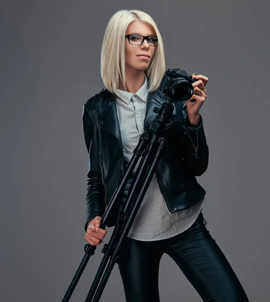 Sexy smarte blonde Fotografin hält eine professionelle Kamera mit Stativ in der Hand und posiert in einem Studio. — Stockfoto