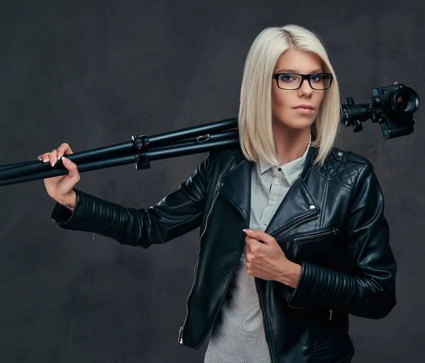 Sexy fotógrafo feminino loira inteligente detém uma câmera profissional com um tripé, posando em um estúdio . — Fotografia de Stock