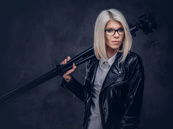 Sexy fotógrafo feminino loira inteligente detém uma câmera profissional com um tripé, posando em um estúdio . — Fotografia de Stock