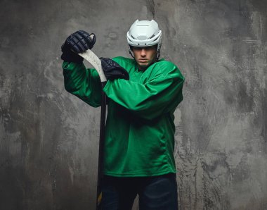 Hokey oyuncusu yeşil koruyucu giysiler ve hokey sopası ile ayakta beyaz kask giyiyor. Gri bir arka plan üzerinde izole. 