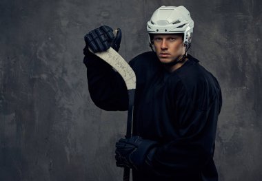 Hokey oyuncusu siyah koruyucu giysiler ve beyaz kask giymiş bir hokey sopası tutar. Gri bir arka plan üzerinde izole.