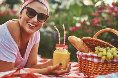 Bir kafa bandı ve açık havada yatarken üzerinde bir battaniyeye bir park piknik sırasında zevk güneş gözlüğü ile rahat kıyafetler içinde mutlu kızıl saçlı orta yaş kadın.