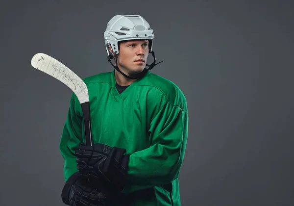 曲棍球运动员穿着绿色防护装备和白色头盔站在灰色背景曲棍球棍 — 图库照片