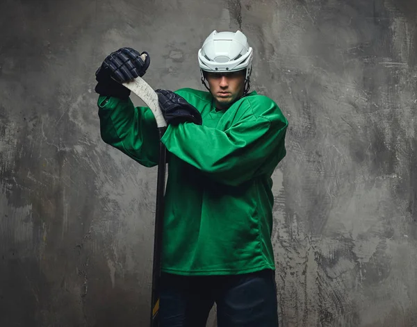 Hokey oyuncusu yeşil koruyucu giysiler ve hokey sopası ile ayakta beyaz kask giyiyor. Gri bir arka plan üzerinde izole. 