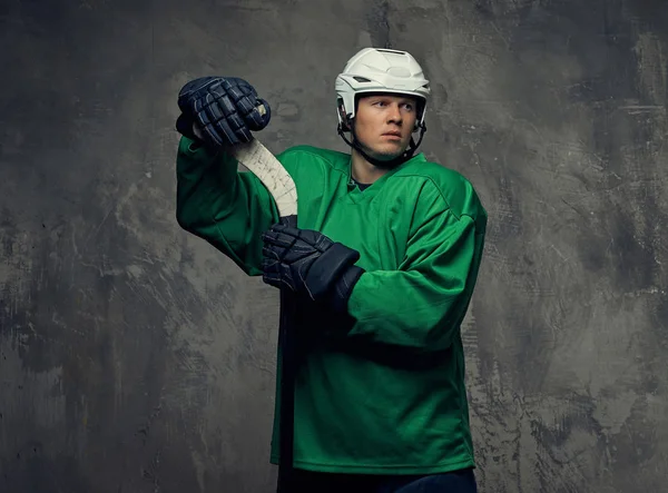 曲棍球运动员穿着绿色防护装备和白色头盔站在曲棍球棒 在灰色背景上隔离 — 图库照片