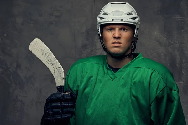 愤怒的职业曲棍球运动员在绿色运动服站在曲棍球棒 在灰色背景上隔离 — 图库照片
