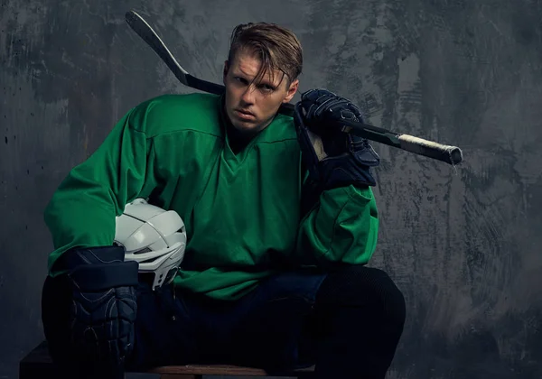 Ahşap palet üzerinde oturan sert bir çalışmadan sonra profesyonel hokey oyuncusu aittir. Gri bir arka plan üzerinde izole.