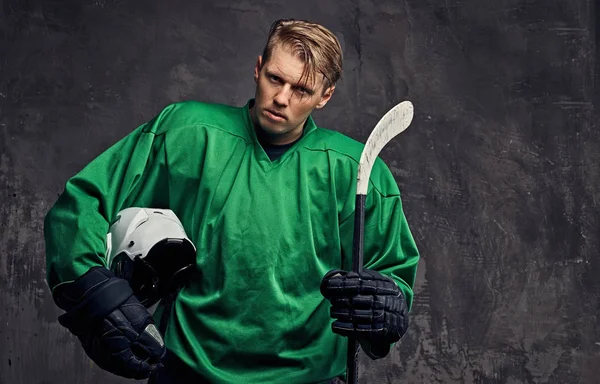 Yeşil bir spor giyim yorgun profesyonel hokey oyuncusu bir hokey sopası ve koruyucu kask tutar. Gri bir arka plan üzerinde izole. 