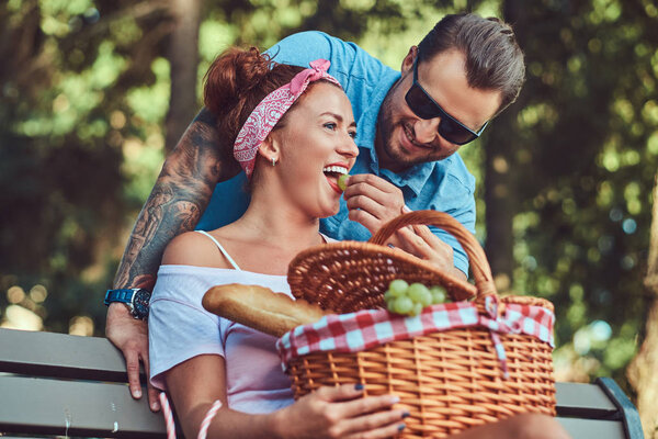 Attractive middle age couple during dating, enjoying a picnic on a bench in the park.