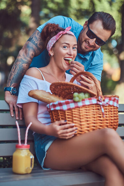 Happy middle age couple during dating, enjoying a picnic on a bench in the park.