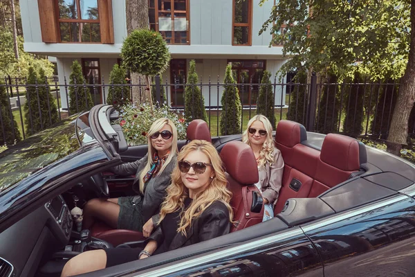 Tatil ve insanlar kavramı. Üç sarışın bayan arkadaşlar tatil yaz cabriolet arabada oturan güneş gözlüğü moda giysiler giyiyor.