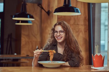 Mutlu genç redhead erkek rahat kıyafetler ve baharatlı Erişte Asya bir restoranda yemek gözlük. 