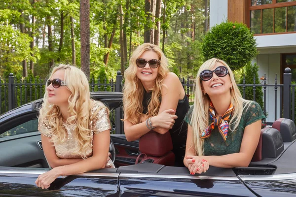 Tatil ve insanlar kavramı. Üç mutlu sarışın bayan arkadaşlar tatil yaz cabriolet arabada oturan güneş gözlüğü moda giysiler giyiyor.