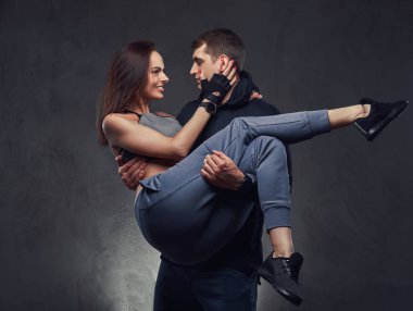 Çekici spor çift. Onun kız arkadaşı spor giyim karanlık dokulu bir arka plan üzerinde giyen ellerinin üstünde yakışıklı adam.