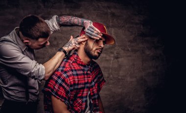 Sakallı Afro-Amerikan hipster adam bir polar gömlek ve bir saç kesimi eski moda bir profesyonel kuaför tarafından getting kap saç kesimi yapıyor.
