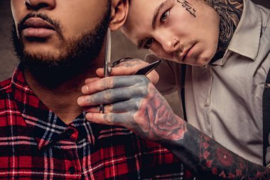 Yakışıklı sakallı Afrikalı-Amerikalı adam bir polar gömlek ve bir saç kesimi eski moda bir profesyonel kuaför tarafından getting kap bir saç kesimi yapıyor.