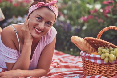 Açık havada yatarken üzerinde bir battaniyeye parkta piknik sırasında bir kafa bandı zevk ile rahat kıyafetler içinde mutlu kızıl saçlı orta yaş kadın.