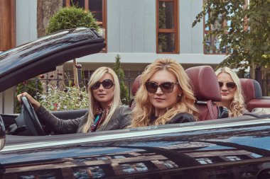 Tatil ve insanlar kavramı. Üç sarışın bayan arkadaşlar tatil yaz cabriolet arabada oturan güneş gözlüğü moda giysiler giyiyor.