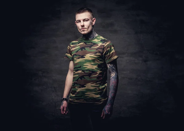 纹身的年轻男子在一个军事 T恤衫的姿势在演播室 在深色纹理背景下隔离 — 图库照片