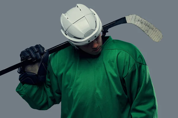 灰色の背景に身に着けている緑の防護服と白いヘルメット立ってアイス ホッケー用スティック ホッケー選手 — ストック写真
